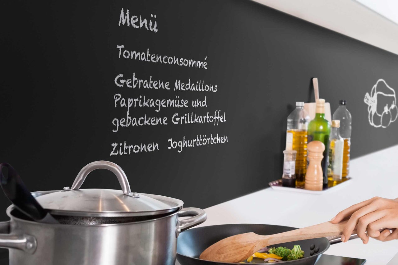 Küchenszene mit Kochtopf, Bratpfanne und handgeschriebener Menütafel
