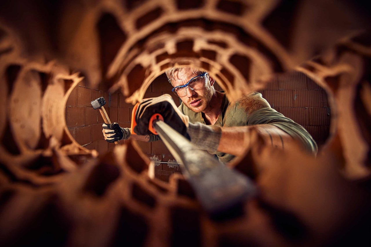 Handwerker bei der Arbeit mit Hammer und Meißel an einer Ziegelwand