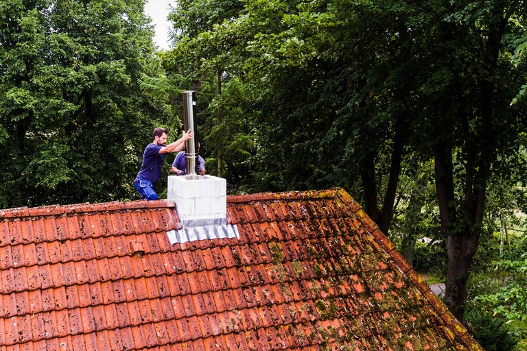 Zwei Handwerker installieren ein Edelstahlrohr auf einem Dach