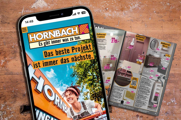 Smartphone zeigt die Webseite des Hornbach Onlineshops mit Badkonzepten und Projektinformationen auf einem Holztisch.