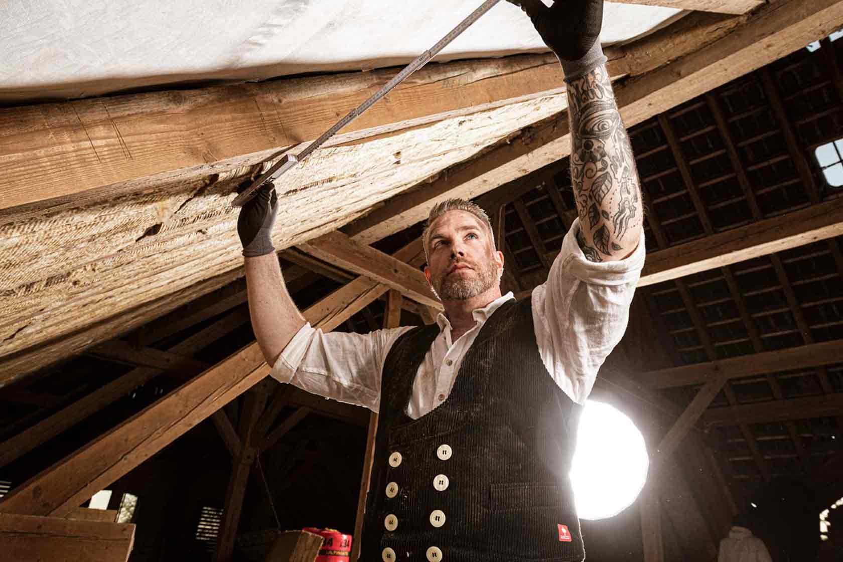 Handwerker misst mit einem Gliedermaßstab einen Dachbalken aus Holz.