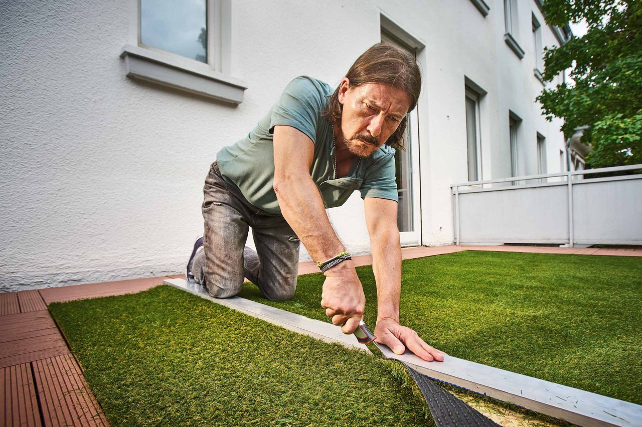 Mann verlegt Kunstrasen auf einem Balkon