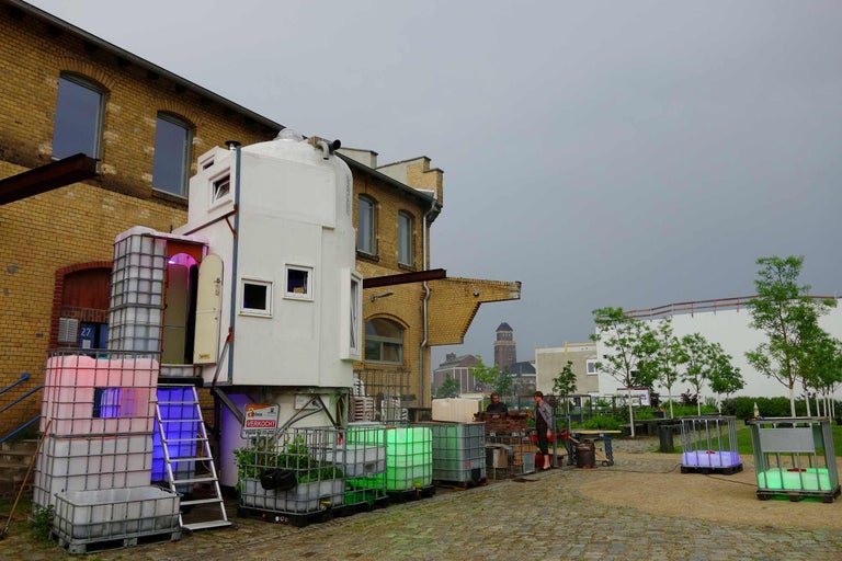 Szene mit einem modularen Haus, das auf Containern steht, und zwei Personen, die im Außenbereich arbeiten