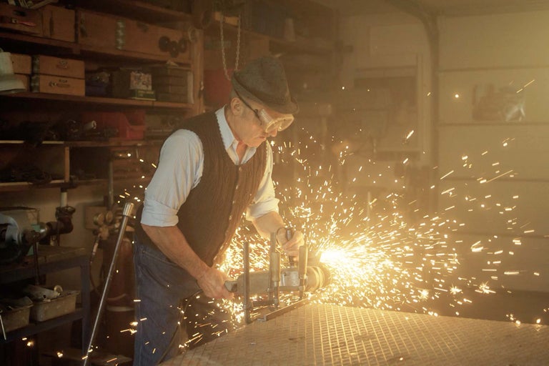 Ein Mann in Schutzbrille bearbeitet Metall mit einem Winkelschleifer, wodurch Funken entstehen.