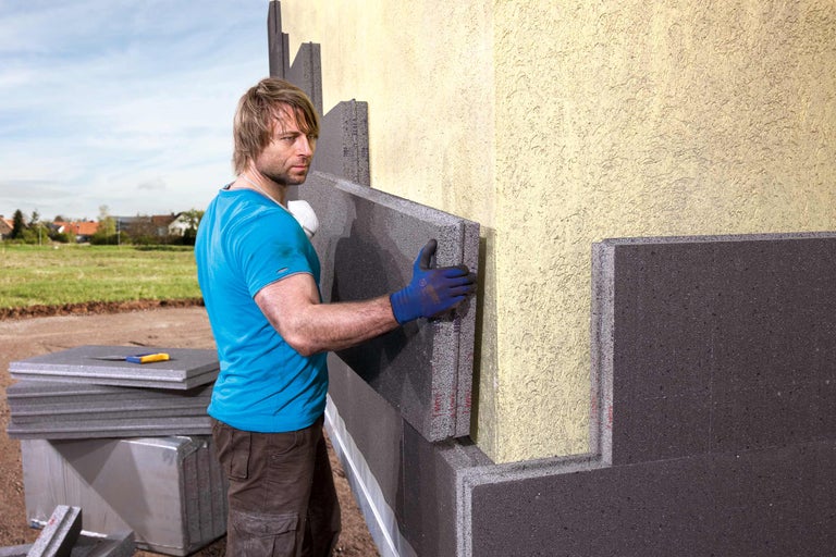Mann bringt Wärmedämmung an einer Hauswand an