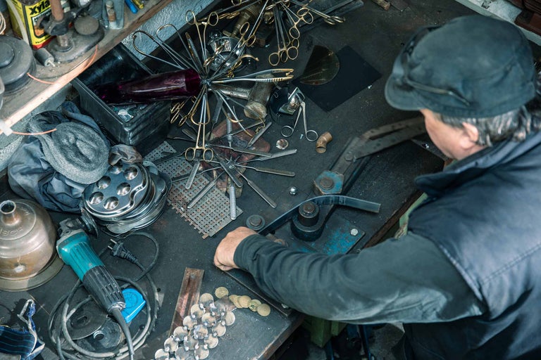 Werkbankansicht mit Werkzeugen, Metallteilen und einer Person, die Metall biegt