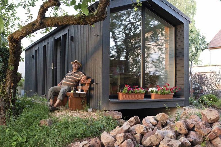 Modernes Gartenhaus mit Mann auf Bank, Blumenkästen und Steinen