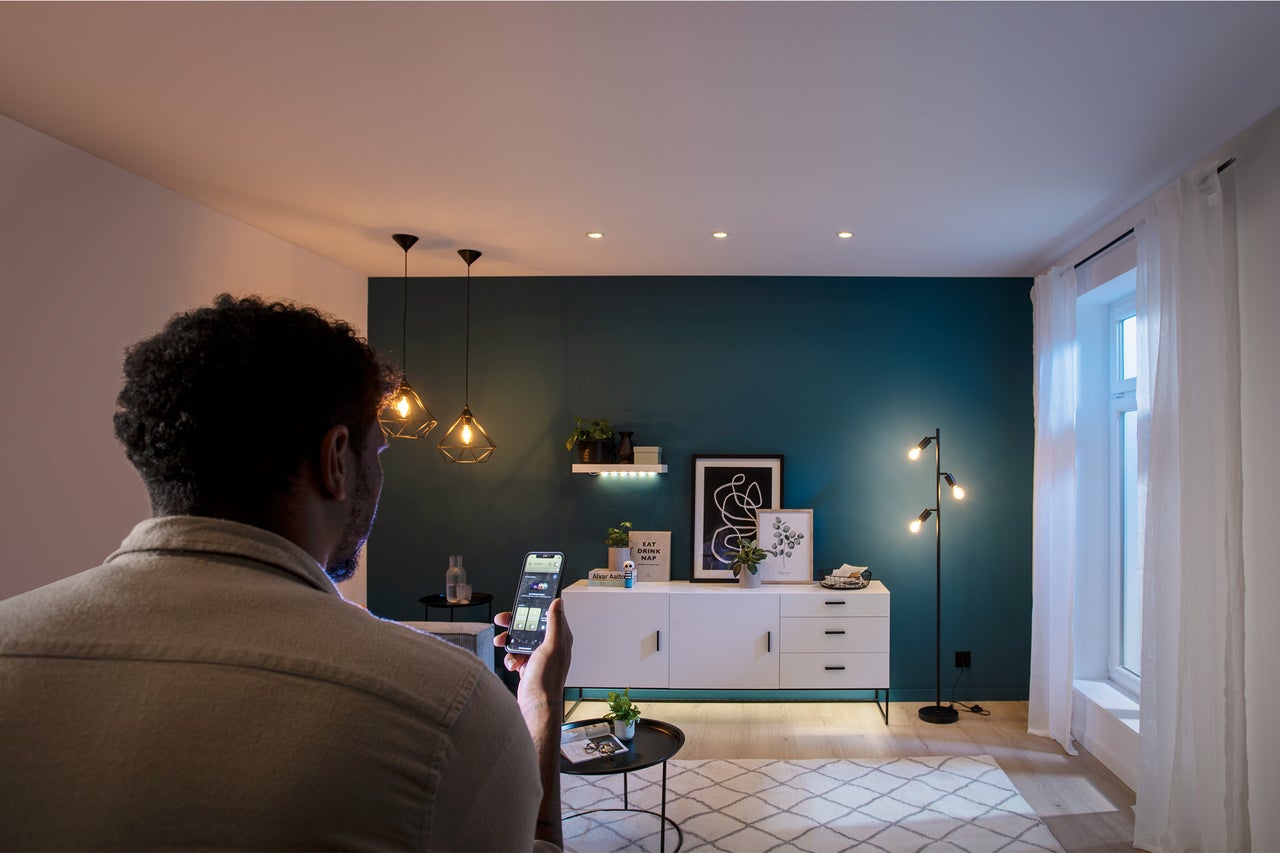 Mann steuert Beleuchtung im Wohnzimmer mit dem Smartphone