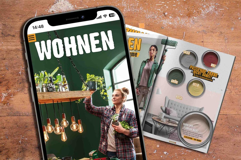 Smartphone mit Anzeige des Hornbach Wohnen-Magazins und Hornbach Farbmischservice-Flyer auf einem Holztisch