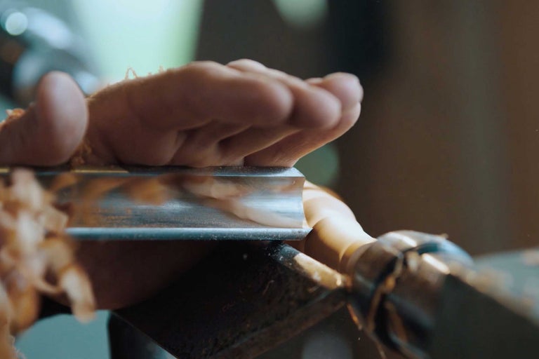 Nahaufnahme einer Hand, die ein Drechseleisen beim Drechseln eines Holzstücks führt.