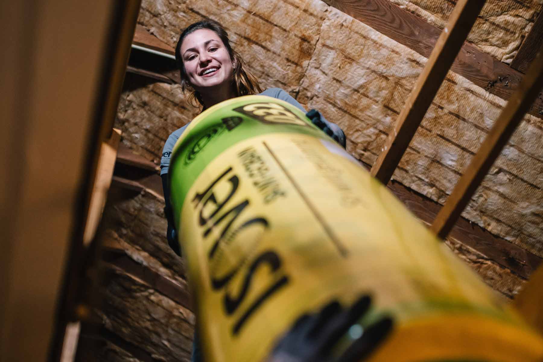 Frau hält Dämmrolle im Dachgeschoss mit Holzrahmen und Dämmmaterial