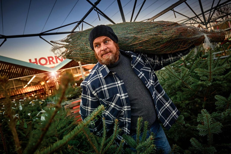 Ein Mann trägt einen verpackten Weihnachtsbaum auf der Schulter in einem Hornbach Markt.