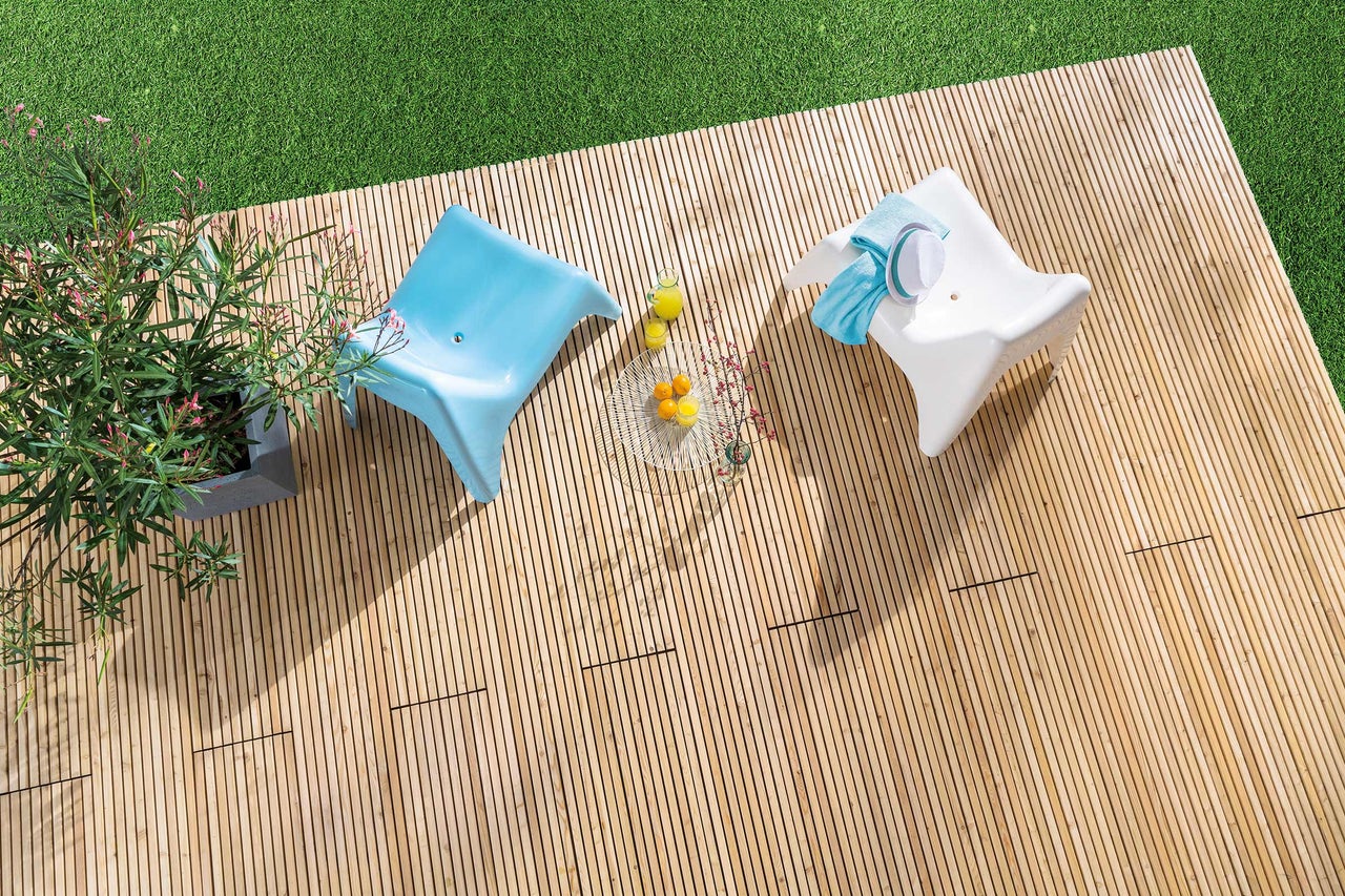 Draufsicht auf eine Holzterrasse mit zwei Stühlen, einem Beistelltisch und einem Topf mit blühenden Pflanzen.