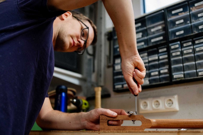 Mann befestigt Mechanik an Gitarrenkopf mit Schraubendreher