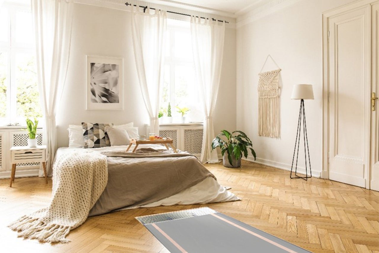 Helles Schlafzimmer mit Bett, Nachttisch, Stehlampe und Teppich auf Parkettboden.
