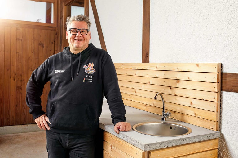 Mann steht neben einer Außenküche mit Spüle und Holzwand