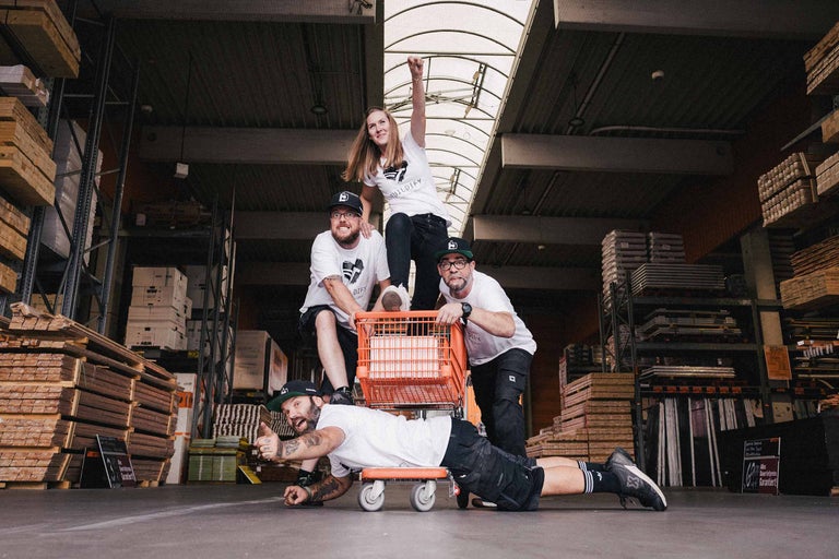 Gruppe von Personen im Hornbach Baumarkt mit einem Einkaufswagen und Bauholz im Hintergrund.