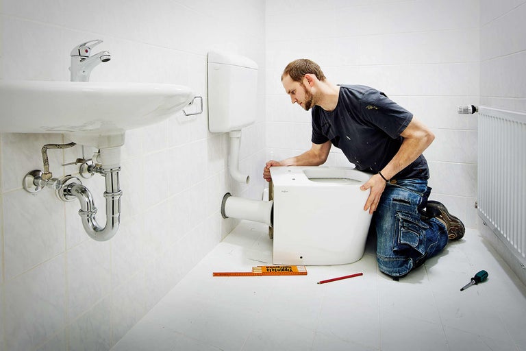 Ein Mann installiert eine Toilette in einem Badezimmer mit Waschbecken und Heizkörper