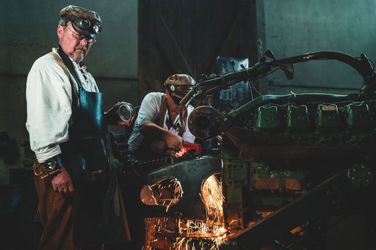 Zwei Männer mit Schweißschutzbrillen arbeiten an einer großen Metallmaschine, wobei Funken fliegen.
