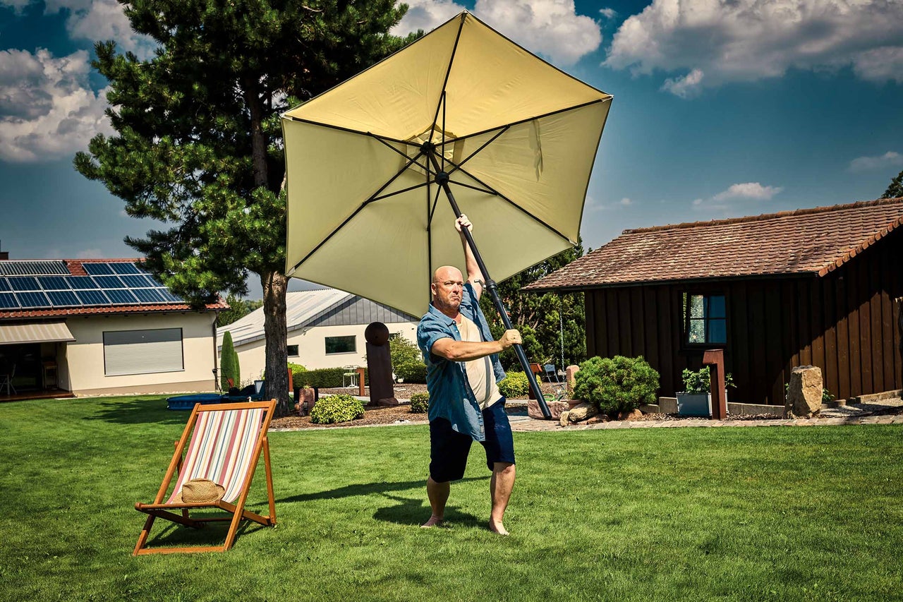 Mann hält Sonnenschirm im Garten.