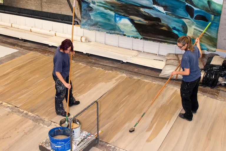 Zwei Frauen tragen mit Flächenstreichern eine Holzschutzlasur auf einen Holzboden auf