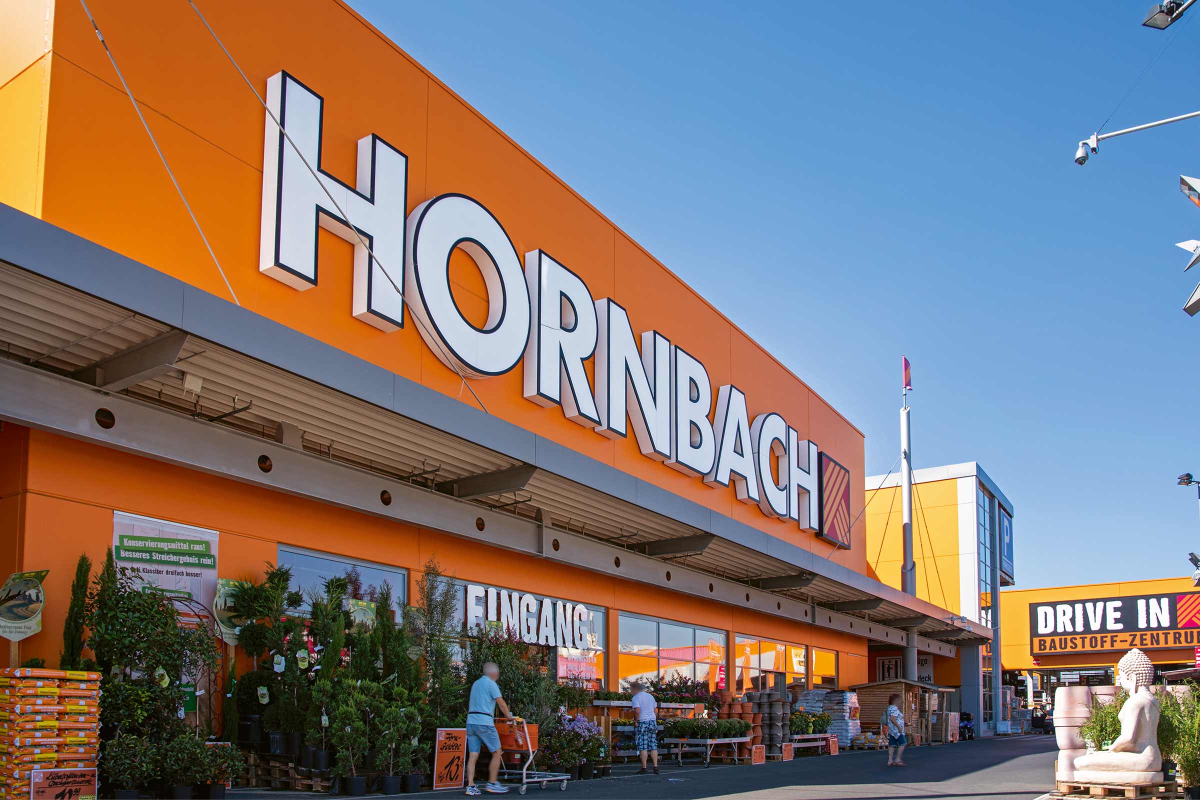  Außenansicht eines Hornbach Baumarktes mit Pflanzen und Einkaufswagen vor dem Eingang. 