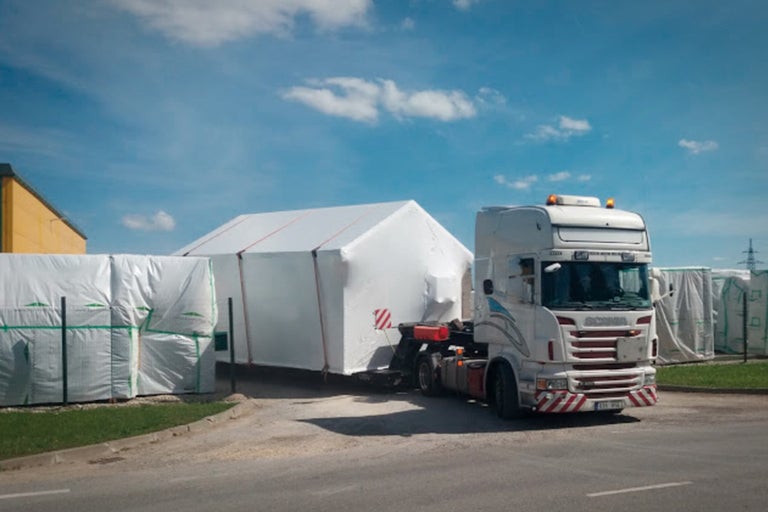 Ein Lastwagen transportiert ein Hausmodul verpackt in Folie.
