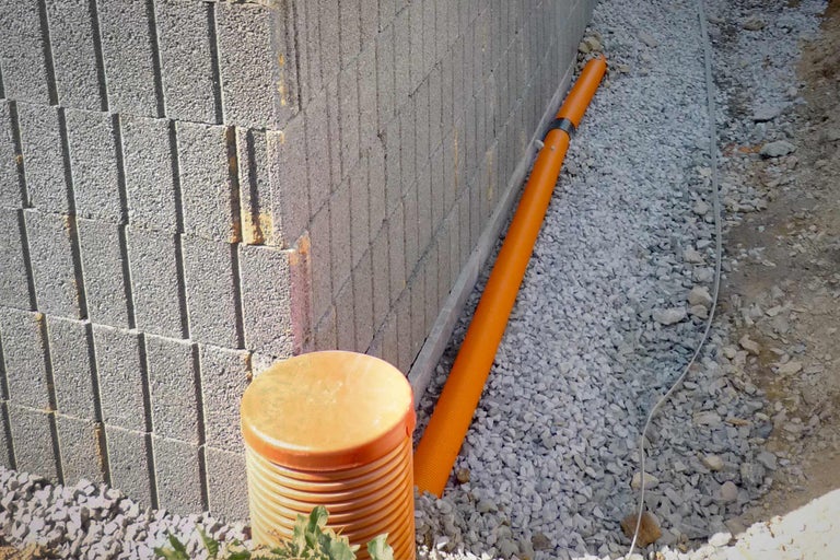Szene mit einem Sickerschacht, einem Drainagerohr und Kies an einer Mauer.