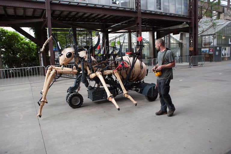 Eine mechanische Spinne mit Sitzen wird von einem Mann mit einer gelben Fernbedienung gesteuert.