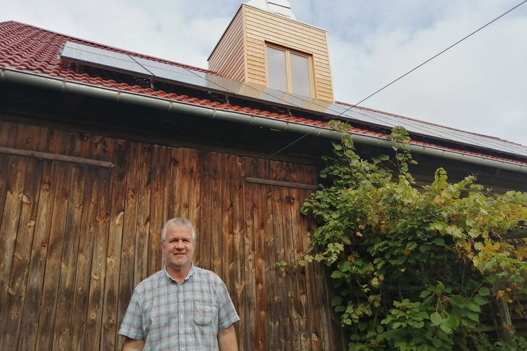Holzscheune mit Solarzellen auf dem Dach und einem Mann im Vordergrund