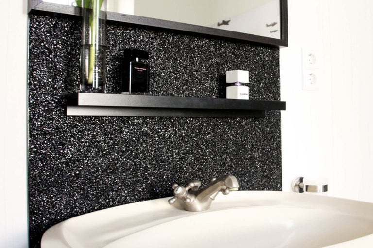 Badezimmerwaschtisch mit Armatur, Spiegel und Wandregal vor glitzernder Wand