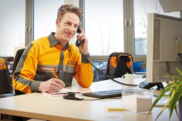 Ein Mitarbeiter von Hornbach telefoniert und macht Notizen an seinem Schreibtisch.