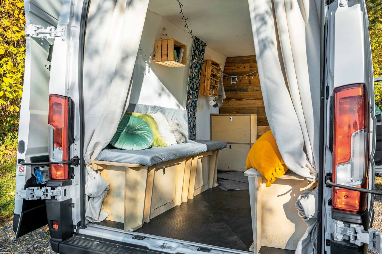 Innenraum eines ausgebauten Kastenwagens mit Holzelementen, Stauraum unter dem Bett und Vorhängen