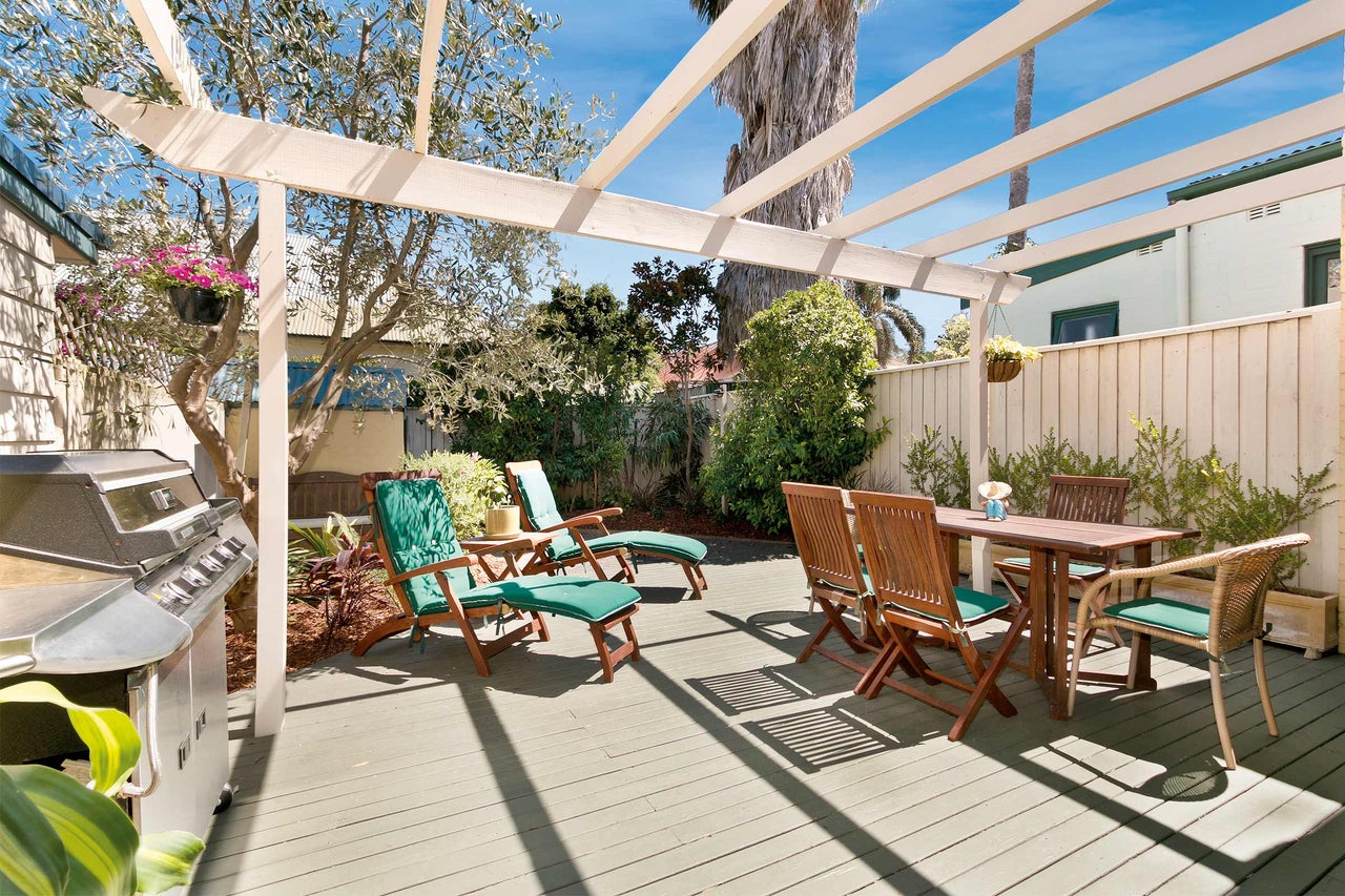 Terrasse mit Grill, Holztisch, Stühlen und Liegestühlen unter einer Pergola