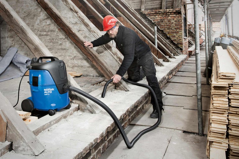 Ein Arbeiter benutzt einen Nass Trockensauger von Nilfisk Alto, um eine Baustelle zu reinigen.