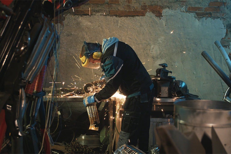 Metallarbeiter mit Schutzmaske beim Schleifen von Metall in einer Werkstatt