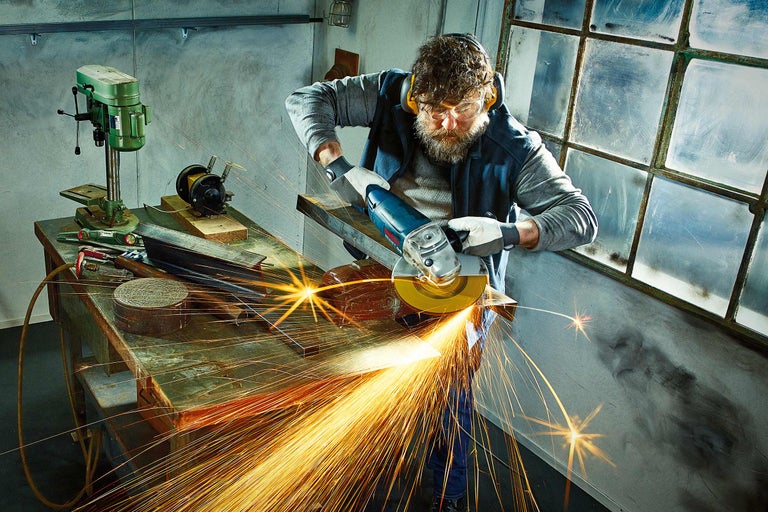 Mann arbeitet mit einem Winkelschleifer in einer Werkstatt und es entstehen Funken.