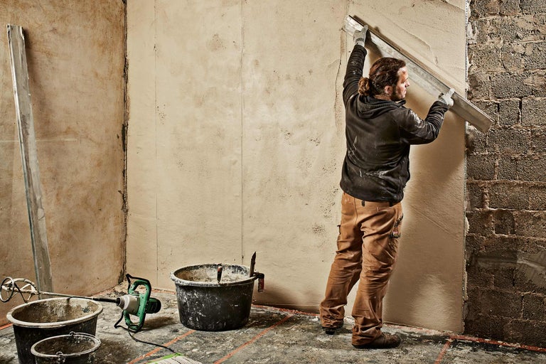 Handwerker glättet Wand mit Putz und Richtscheit in einem Raum