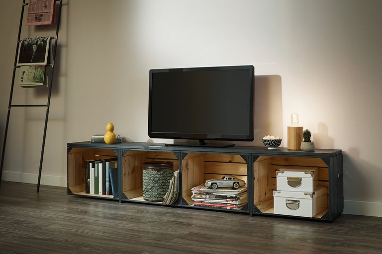 Wohnzimmer mit Fernsehgerät auf einem Lowboard aus Holzkisten und Zeitungsständer.