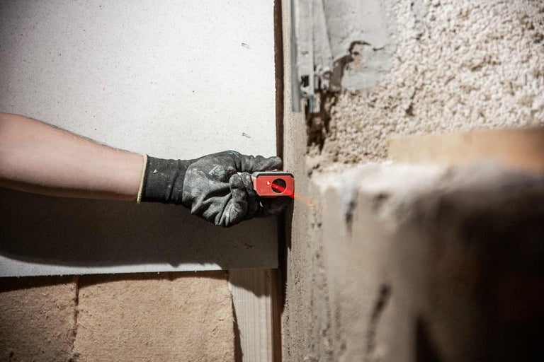 Hand mit Arbeitshandschuh verwendet eine Laserwasserwaage an einer Wand.