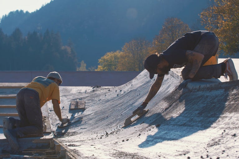 Zwei Bauarbeiter glätten Beton mit Glättkellen auf einer Baustelle.