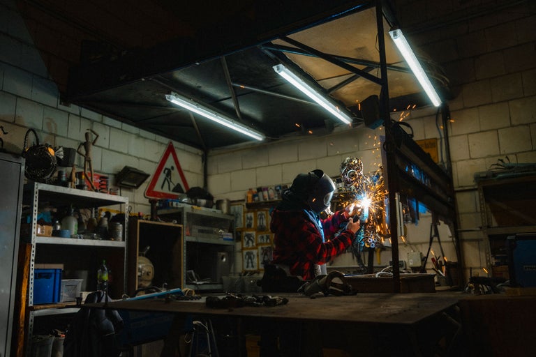 Werkstattansicht mit Schweißer, der mit Schutzkleidung arbeitet und Funken erzeugt.