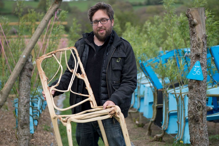 Mann hält einen Stuhl aus Holz in einem Garten.