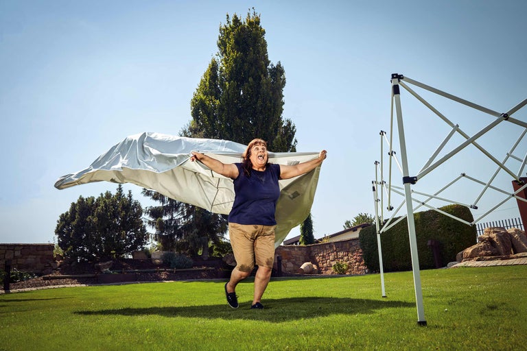 Eine Frau im Garten hält eine Zeltplane hoch, neben einem Pavillon.