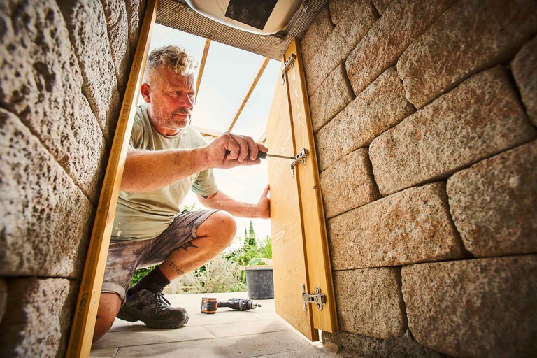 Mann montiert eine Holztür in einer Mauer mit einem Schraubenzieher