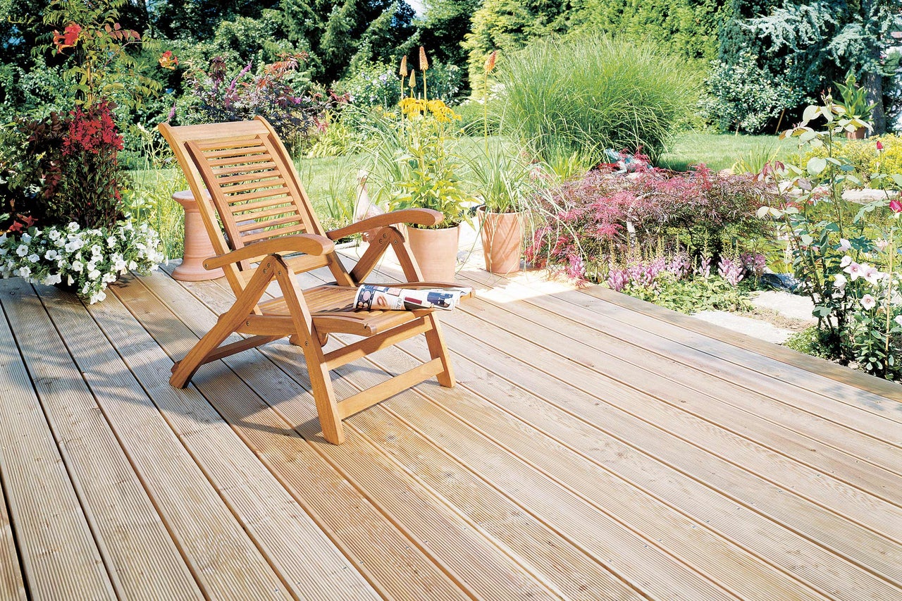 Holzterrasse mit Gartenliege und Blumenbeeten im Garten