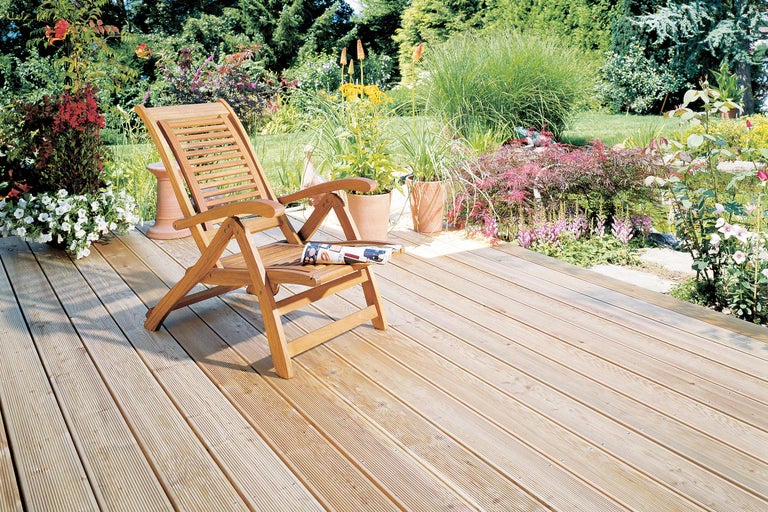 Holzterrasse mit Gartenliege und Blumenbeeten im Garten