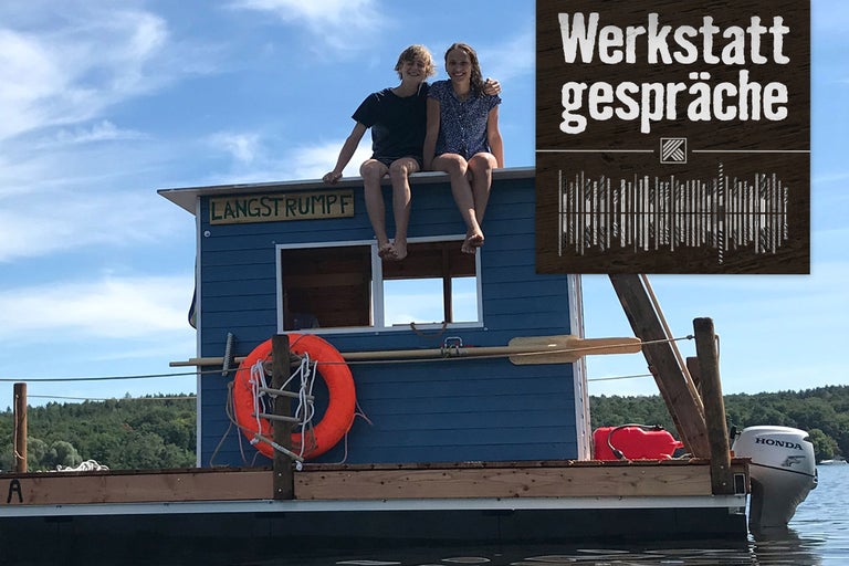Zwei Personen sitzen auf einem blauen Hausboot mit dem Namen Langstrumpf auf einem See. Im Hintergrund befindet sich das Logo von Werkstattgespräche.