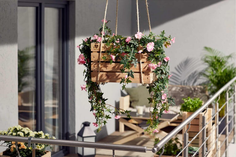 Hängender Holzkasten mit rosa Blüten und grünen Blättern für den Außenbereich.