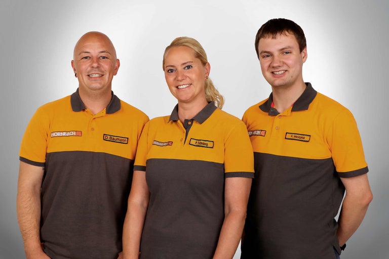 Drei Hornbach Mitarbeiter in Arbeitskleidung posieren für ein Foto.